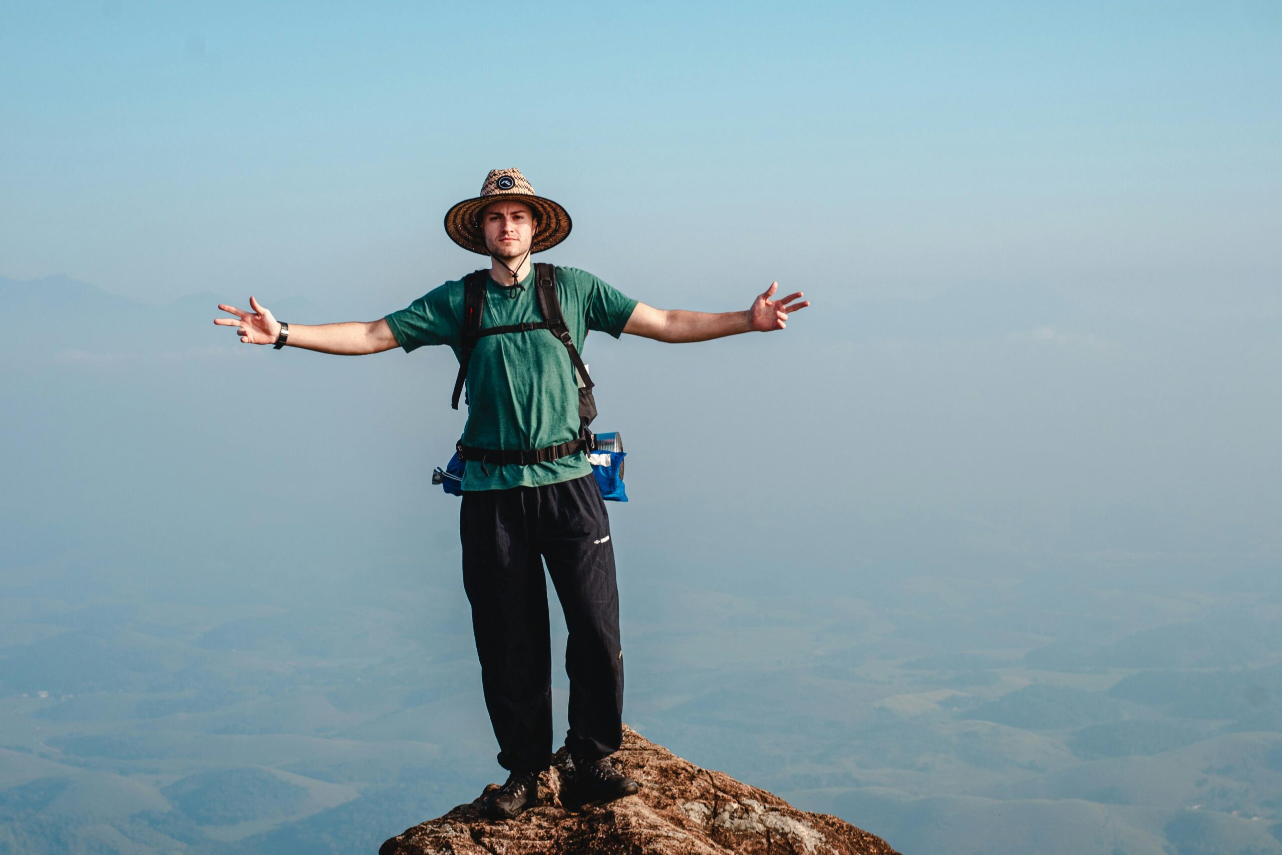 Man with arms outstretched stands on a mountain peak, enjoying scenic views.